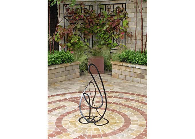 The paved labyrinth design is re-imagined as a 3-dimensional sculpture and also in the steel trellis