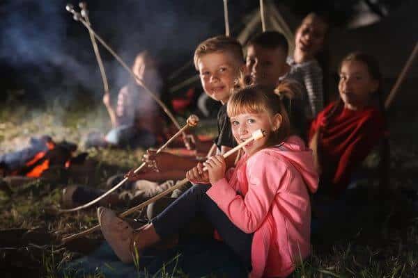 Smiling kids sit round a campfire toasting marshmallows